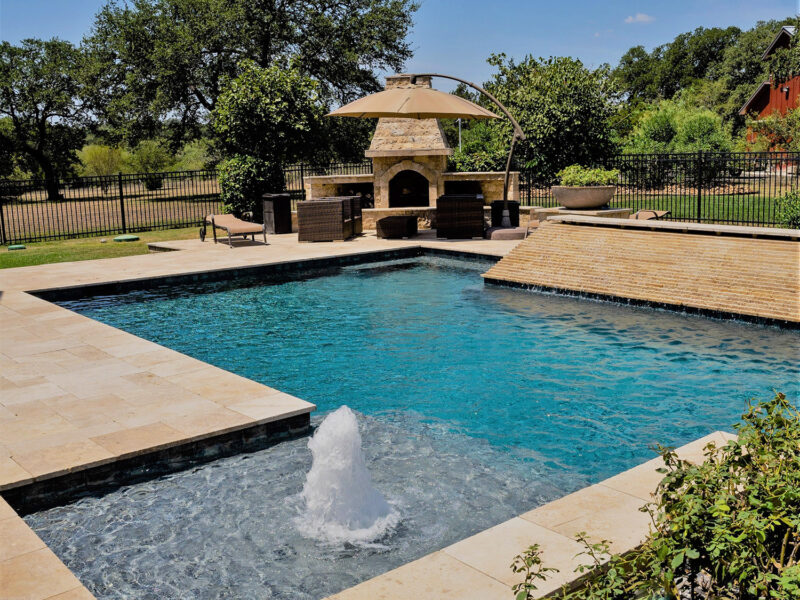 This modern geometric pool features an outdoor fireplace, sheer descent, and stunning water features.