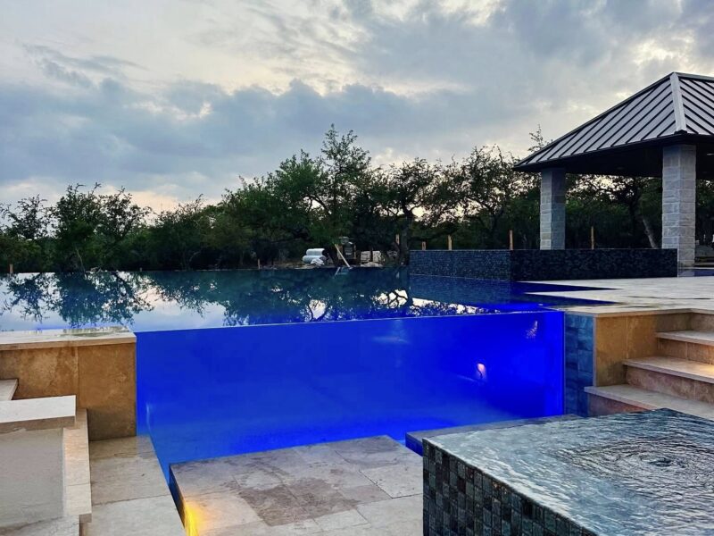 Luxury negative-edge pool with illuminated blue acrylic edge, elevated spa, and modern Hill Country cabana by Infinity Pools Texas